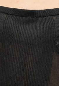 Κοντινό πλάνο ενός ατόμου που φοράει μαύρο ριμπ πλεκτό πουλόβερ με στρογγυλή λαιμόκοψη σε ουδέτερο φόντο.