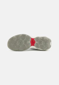 Suela de zapatillas deportivas con una base de goma con un patrón en gris claro, acento rojo y un diseño texturizado para proporcionar tracción.