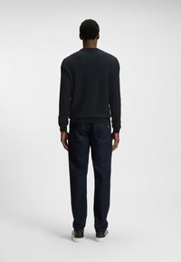 Black textured sweater with a crew neck, paired with dark blue straight-leg jeans and black leather sneakers. Rear view showcases overall fit.