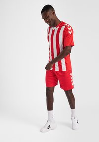 Rød- og hvidstribet atletisk trøje med korte ærmer, parret med ensfarvede røde shorts. Bæres med hvide sneakers og sokker i ankellængde.