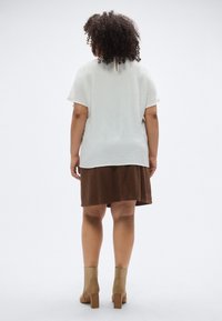 Λευκό υφασμάτινο τοπ, καφέ βελούδινη φούστα, μπεζ μπότες μέχρι τον αστράγαλο με χοντρό τακούνι. Οπίσθια όψη παρουσιάζει το στρωμένο σχέδιο της ενδυμασίας.