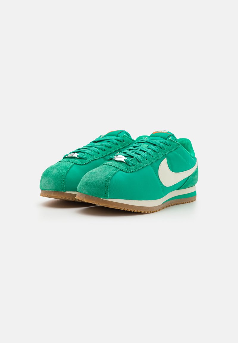 Zapatillas verdes con materiales de ante y sintéticos, presentando un swoosh blanco, cordones texturizados y una suela de goma, diseño de corte bajo.