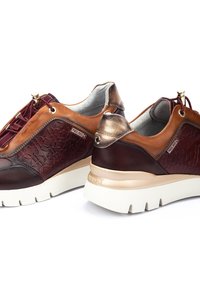 Chaussures marron et bordeaux en cuir texturé, avec des accents métalliques, des côtés à motifs et des semelles blanches rembourrées. Comprend un système de laçage.