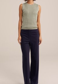 Ljust grön ribbad ärmlös topp i kombination med mörk marinblå vida byxor, som har en knappdetalj i midjan och en slät textur.