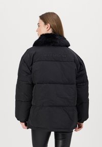 Black puffer jacket with a detachable faux fur collar, quilted design, and subtle logo embossed on the back. Smooth texture, long sleeves.