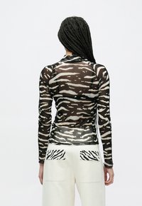 Sort og cremefarvet gennemsigtig bluse med lange ærmer og tigerstribet mønster, kombineret med hvide bukser med matchende lommeaccenter.