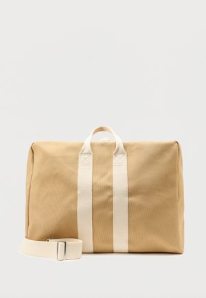 Geantă de voiaj dreptunghiulară din pânză bej, cu două mânere verticale albe și o curea de umăr albă reglabilă, pe un fundal simplu deschis.