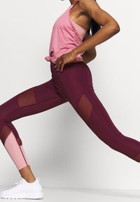 Burgundin korkea vyötärö leggingsit, joissa on verkkosivupaneelit, yhdistettynä vaaleanpunaiseen toppiin. Asu on muotoiltu istuvaksi ja siinä on teksturoitu kangas.