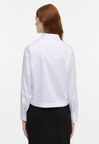 Witte cropped shirt met lange mouwen, fitted kraag en knoopdetails op de manchetten. Gladde textuur, minimalistisch ontwerp en op maat gemaakte pasvorm.