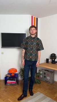 Μπλουζάκι κοντού μανικιού με γεωμετρικό μοτίβο σε πράσινο, καφέ και μπλε χρώμα; συνδυασμένο με σκούρες μπλε τζιν παντελόνες και καφέ λουστρίνια; εσωτερικό περιβάλλον.