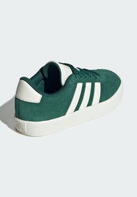 Zapatillas verdes de ante con suela de goma blanca, con tres rayas blancas y cuello acolchado. Diseño sencillo con un acabado texturizado.