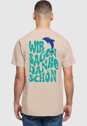 Beige T-Shirt mit auffälligem türkisfarbenem und blauem Text "WIR SAGEN DANKE SCHÖN" und einem Delfin-Graphic. Kurze Ärmel und lockere Passform.