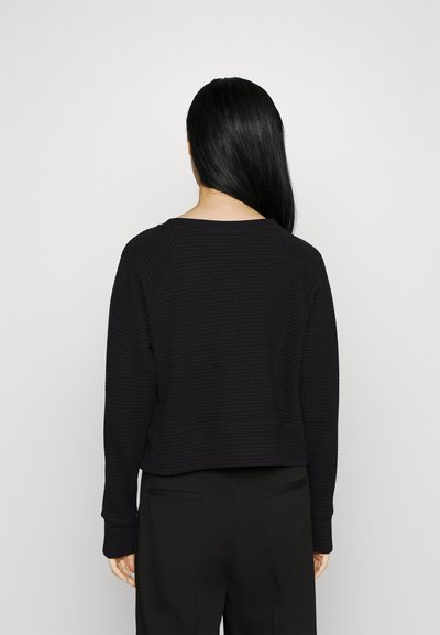 Maglione nero, texturizzato, con un design cropped, scollo ampio e maniche raglan. Abbinato a pantaloni neri su misura con una vestibilità rilassata.