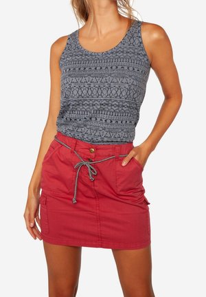Femme portant un débardeur gris à motifs sans manches rentré dans une jupe rouge à boutons sur le devant avec une ceinture à cordon nouée.