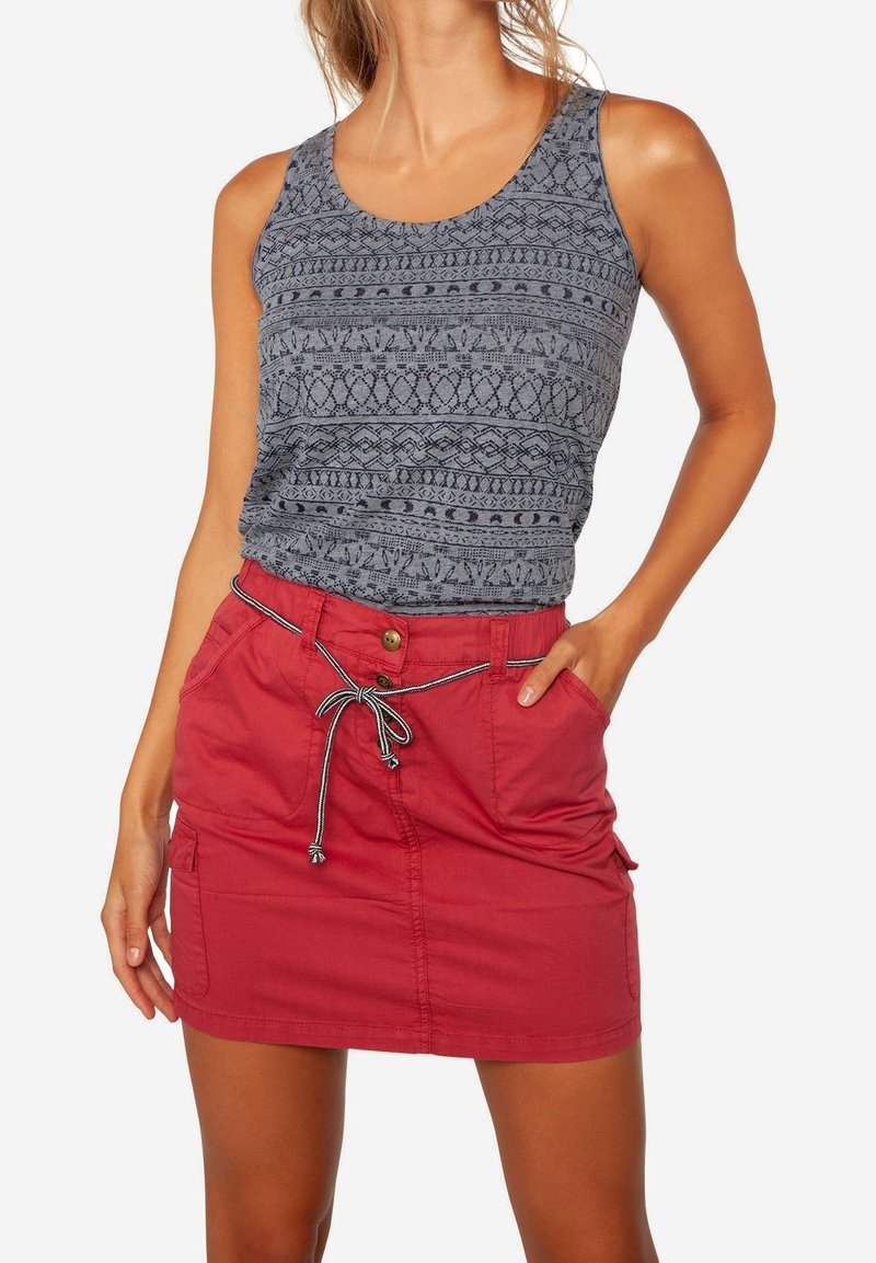 Femme portant un débardeur gris à motifs sans manches rentré dans une jupe rouge à boutons sur le devant avec une ceinture à cordon nouée.