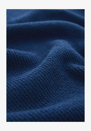 Sötétkék textília, texturált, bordázott felülettel, amely lágy, szőtt szálakat és finom árnyalatbeli eltéréseket mutat.