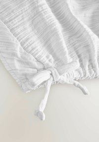 Tissu blanc texturé avec des rayures subtiles. Doté d'une fermeture à cordon avec des extrémités nouées. Matériau lisse et léger.