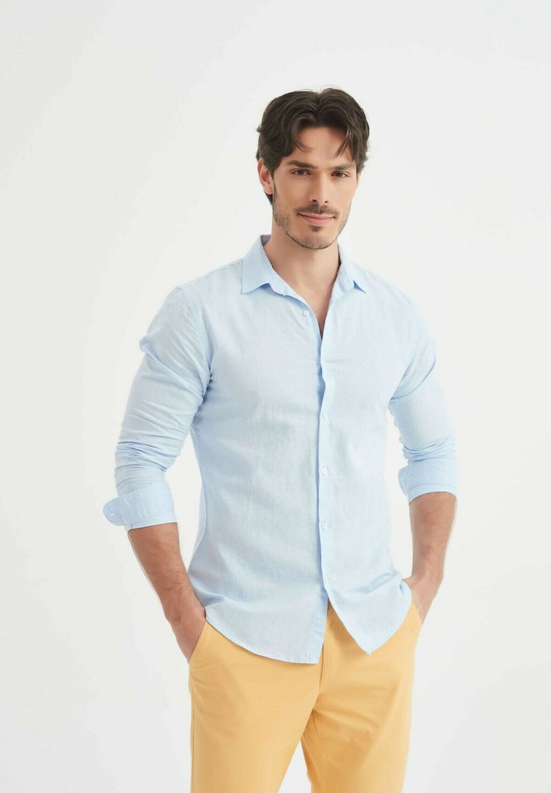Chemise bleu clair à boutons avec des manches longues, associée à un pantalon jaune. La chemise a un col et une coupe décontractée.