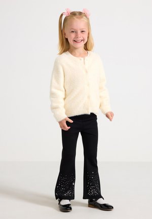 Fluffy cream cardigan with buttons, paired with black flared pants featuring silver sequin detailing at the hem. Black patent shoes.