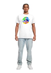Hvid bomulds t-shirt med et farverigt fredssymbol grafisk design omgivet af sprøjt af grøn, blå og orange; parret med lyseblå jeans.