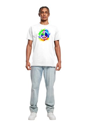 Hvid bomulds t-shirt med et farverigt fredssymbol grafisk design omgivet af sprøjt af grøn, blå og orange; parret med lyseblå jeans.