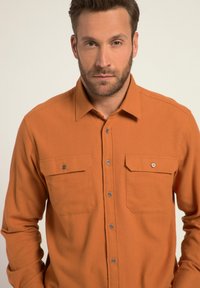 Orange Langarmhemd aus strukturiertem Stoff. Verfügt über einen Kragen, eine Knopfleiste, zwei Brusttaschen und sichtbare Metallknöpfe.