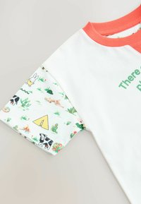 Bela kratka bombažna majica s kratkimi rokavi z oranžnim rebrastim ovratnikom, na rokavih je pisana živalska oblika, na prednji strani pa je zeleno besedilo.