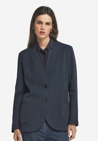 Marinblå blazer av texturerat tyg, utan krage, med två framfickor och två stora svarta knappar för stängning.