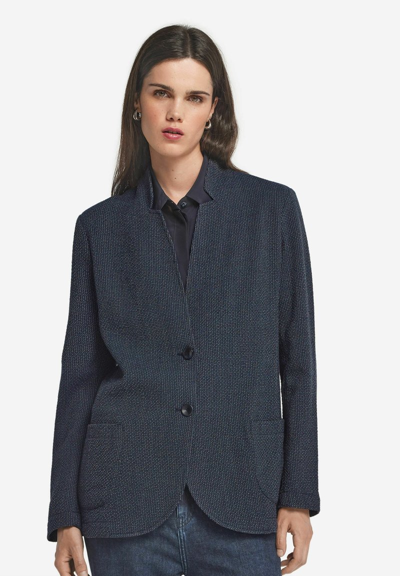 Marinblå blazer av texturerat tyg, utan krage, med två framfickor och två stora svarta knappar för stängning.
