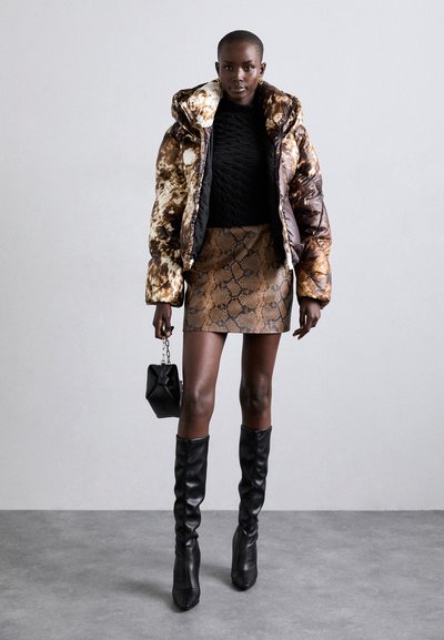 Jachetă puffer cu model maro și negru, pulover negru texturat, fustă mini cu imprimeu de șarpe, cizme cu toc negre până la genunchi și o geantă mică neagră.