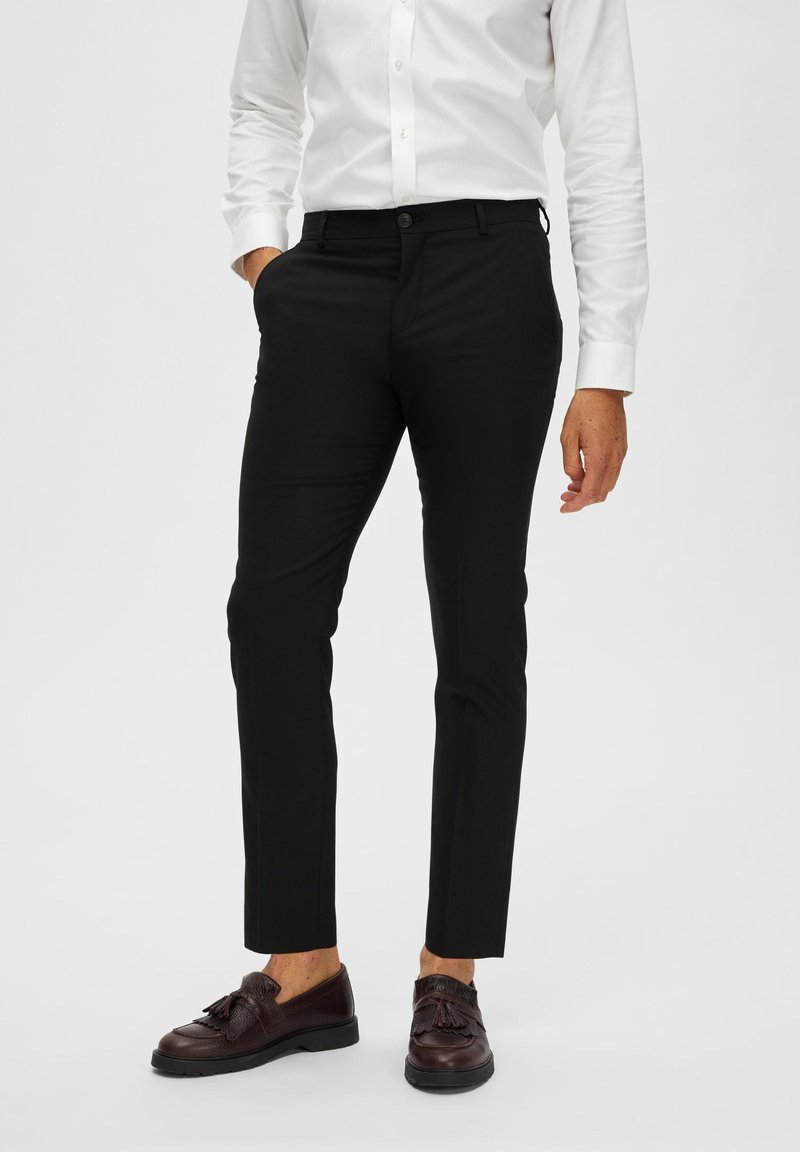 Svarta skräddarsydda byxor i en slät tygkvalitet, slim fit, med sidofickor och knappstängning, i kombination med bruna strukturerade skor.