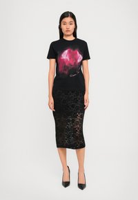 Black graphic T-shirt with pink abstract design, paired with a black lace midi skirt and pointed black heels.