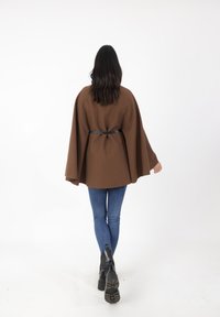 Brun kappa i texturerad tyg, midjebältad med ett svart band, i kombination med blå jeans och svarta ankelstövlar.