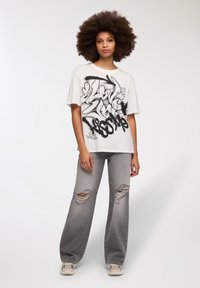 Krótki rękaw, luźna biała koszulka z czarnym nadrukiem graffiti, zestawiona z spodniami dżinsowymi w jasnoszarym kolorze z wysokim stanem i neutralnymi sneakersami.