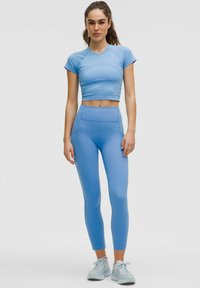 Lichtblauw crop top voor sport met ribbeltextuur, gecombineerd met bijpassende high-waisted legging. Model draagt lichtblauwe sneakers.