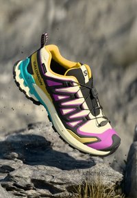 Chaussure de course Salomon avec un col jaune, des accents noirs et violets, une tige en maille, une semelle turquoise épaisse et un design superposé pour un soutien.