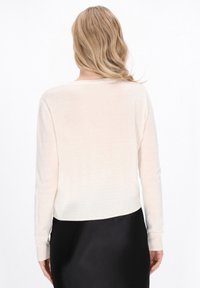 Hellbeige Pullover, weiche Textur, lange Ärmel, runder Halsausschnitt, verkürzte Passform. Trifft auf einen glatten schwarzen Rock. Subtile Strickmuster.