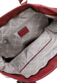 Interno di una borsa in pelle rossa con fodera grigia, caratterizzata da un motivo geometrico bianco. Include una tasca con zip e un'etichetta piccola.