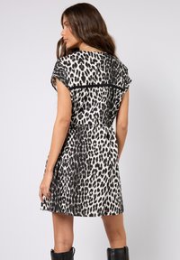 Krótka sukienka z czarno-białym wzorem w cętki lamparta, krótkimi rękawami, dopasowaną talią i luźną spódnicą. Tkanina o wyraźnej fakturze z gładkim wykończeniem.