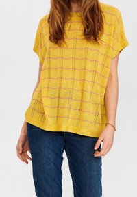 Gul stickad topp med korta ärmar, med ett strukturerat mönster av rosa ränder och små öppna stygn, kombinerad med mörkblå jeans.