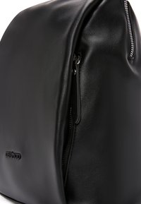 Zaino in pelle nera con forma arrotondata, texture liscia e chiusura con zip laterale. Presenta dettagli con logo in rilievo.