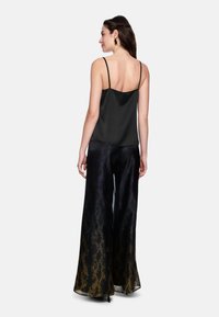 Black satin camisole with thin straps, paired with wide-legged black pants featuring a gradient snake print in purple and gold.