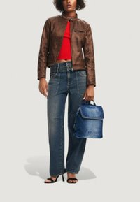 Braune Kunstlederjacke, rotes kurzes Oberteil, hochgeschnittene blaue Jeans und ein blauer Denim-Rucksack. Offenporige schwarze Absätze vervollständigen den Look.