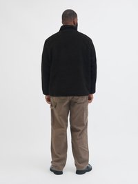 Czarna polarowa kurtka z wysokim kołnierzem, zestawiona z beżowymi spodniami cargo. Kurtka posiada miękką teksturę i luźny krój. Czarne obuwie.