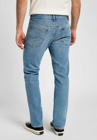 Ljusblå denim jeans med rak passform, som har bakfickor och en beige läderetikett vid midjan. Bärs tillsammans med svarta sneakers.