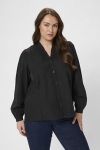 Blusa negra de botonadura con un escote en V con volante, mangas largas con puños fruncidos y ajuste relajado. Llevada con jeans azul oscuro.