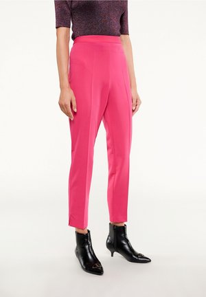 Woman wearing bright pink high-waist tapered pants paired with black pointed-toe ankle boots and a short-sleeve textured top.