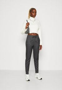 Pull à col roulé blanc côtelé, coupe courte. Pantalon à rayures gris foncé avec taille à cordon. Sac gris et baskets blanches.