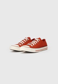 Czerwone zamszowe sneakersy z białymi sznurówkami, gumowymi noskami i tonową podeszwą z dwoma czerwonymi paskami. Niski profil.