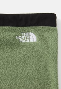 Tissu polaire vert avec des bordures noires et le logo brodé "The North Face" en blanc près du haut au centre.